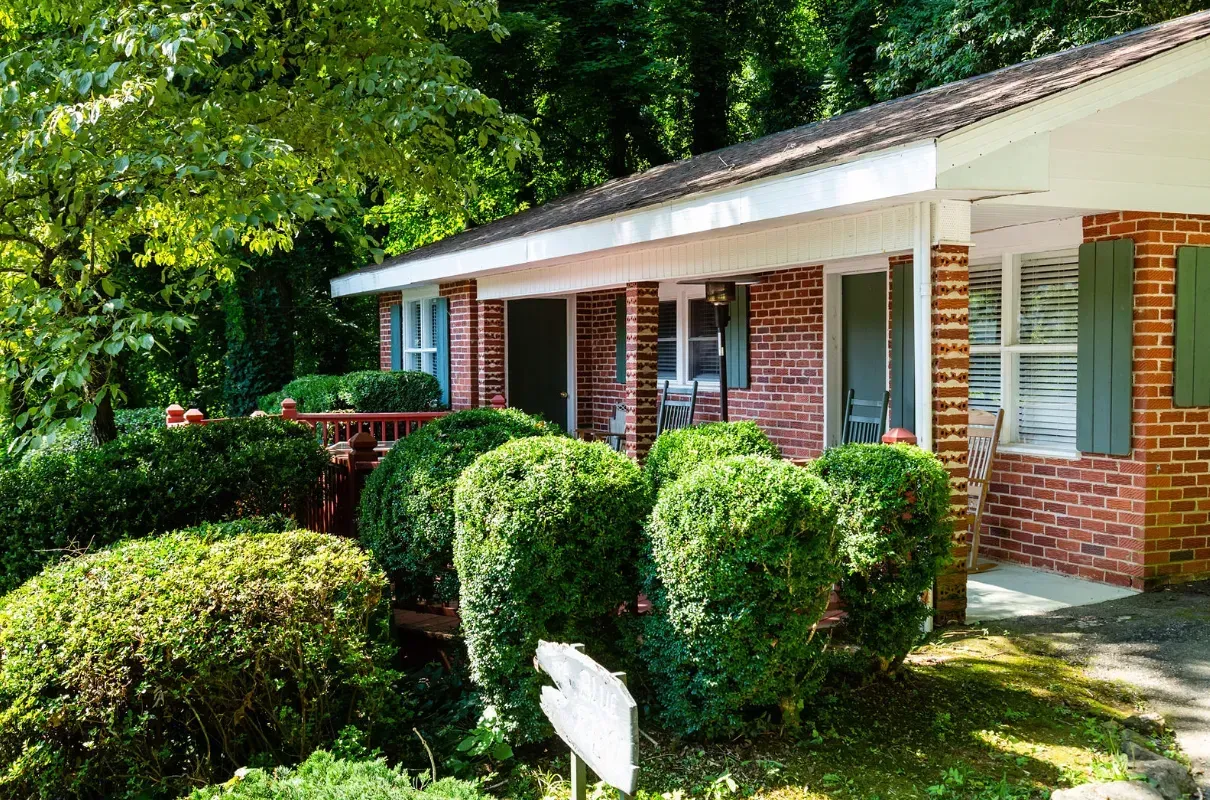 Red brick house with green shutters and manicured bushes in front.