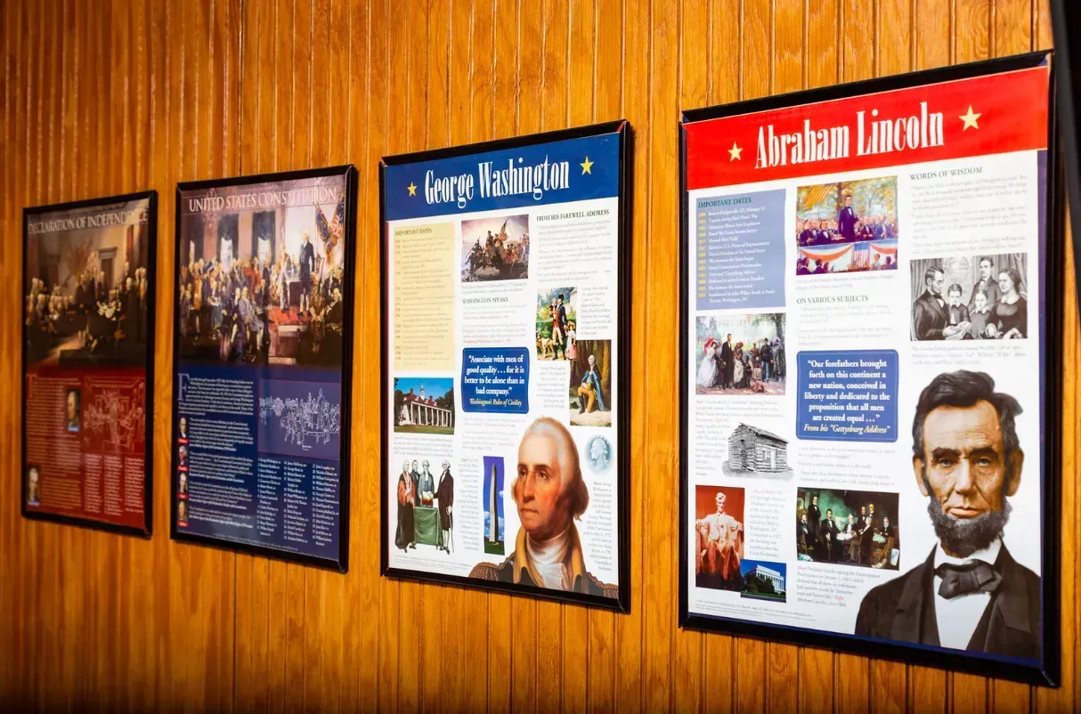 Posters of U.S. presidents, George Washington and Abraham Lincoln, on wood-paneled wall.