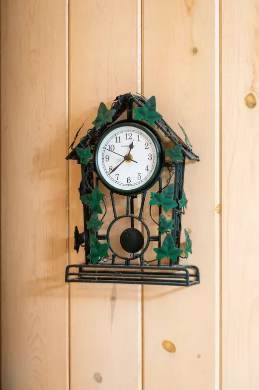 Black and green metal clock with ivy on a light wooden wall.