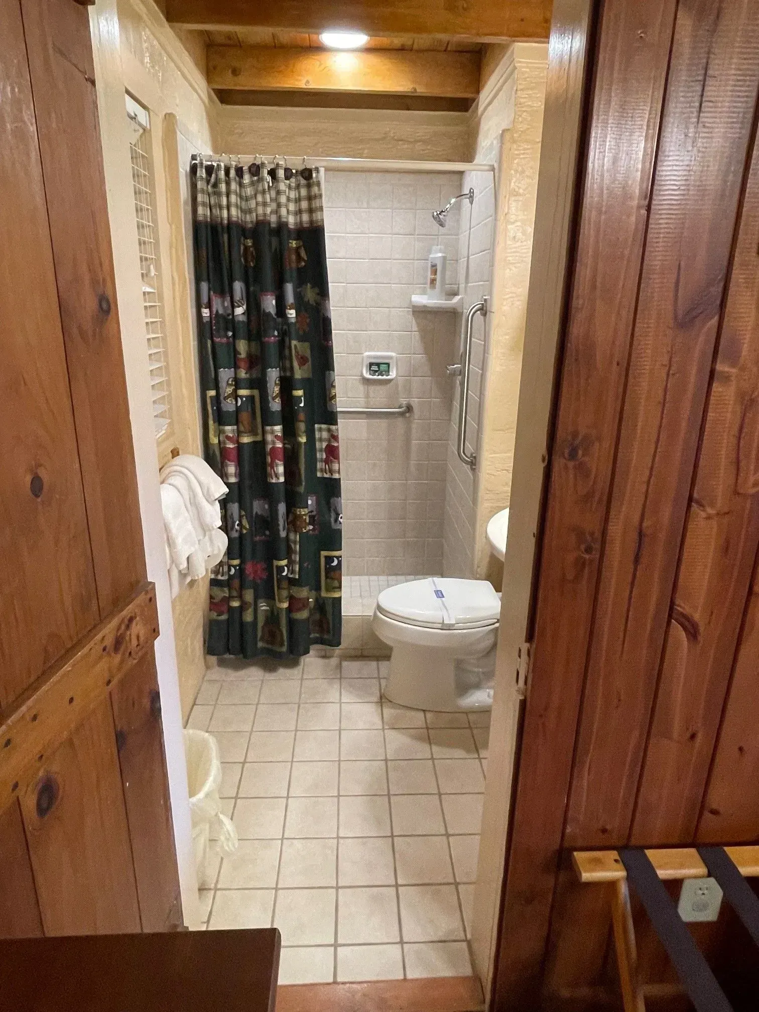Bathroom with tiled floor, shower, toilet, and wooden door.