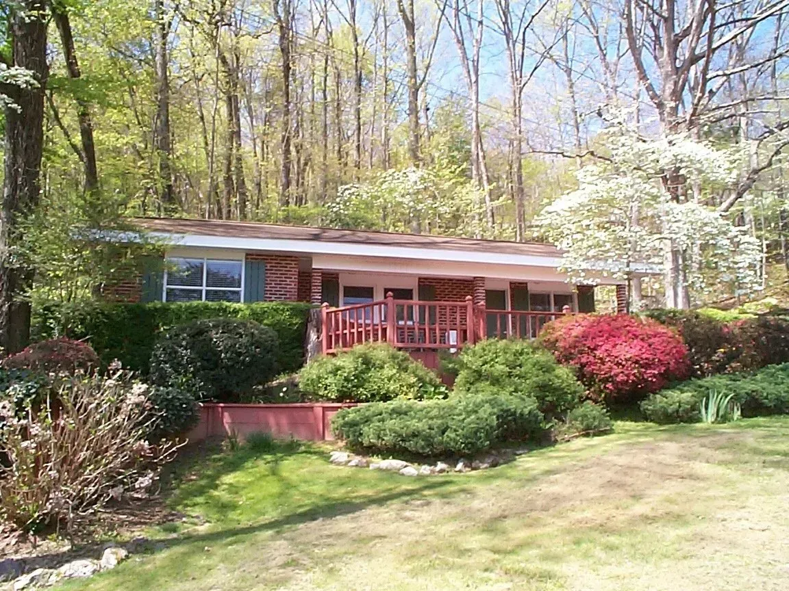 Ranch home with a red deck and landscaping, set against a backdrop of trees.