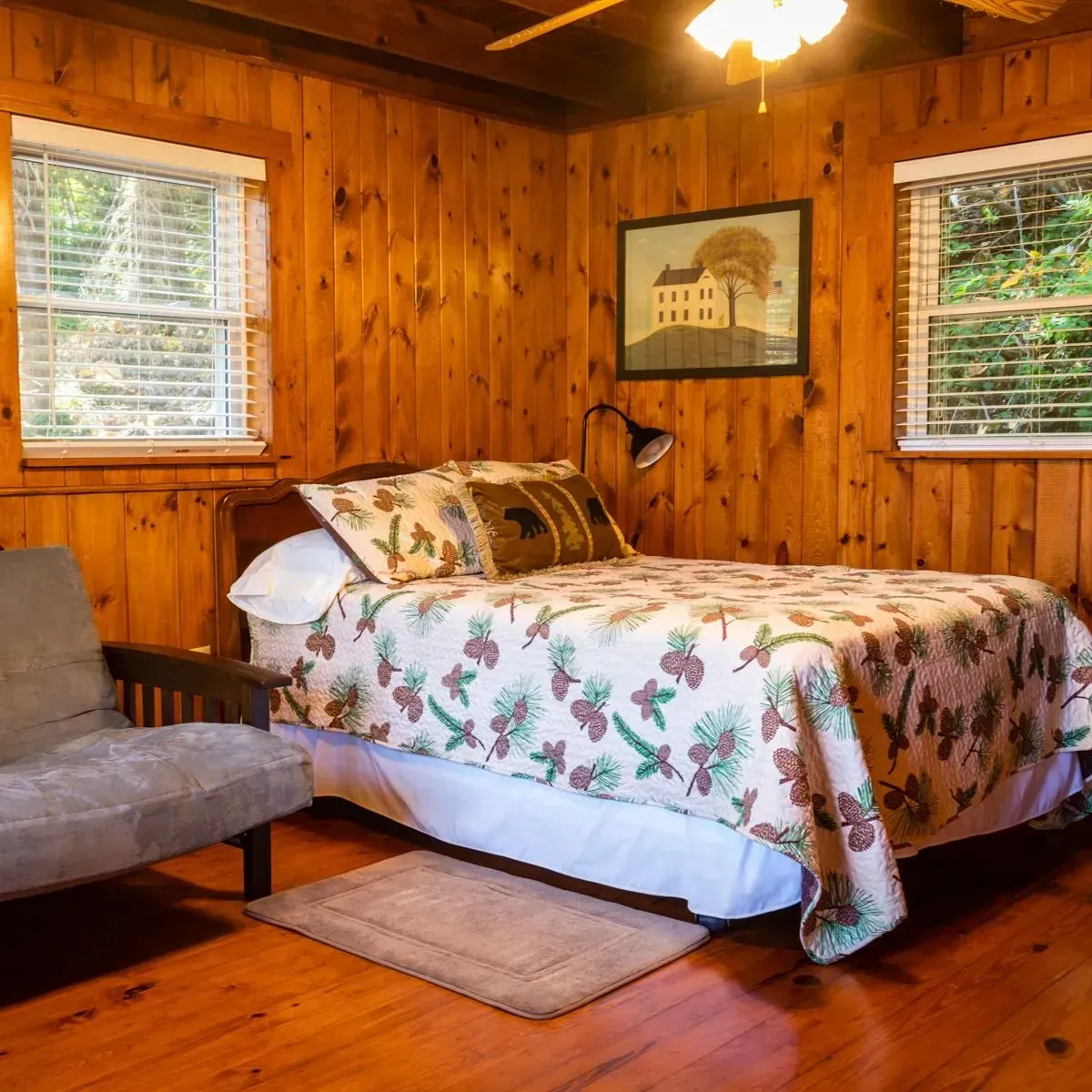 Bedroom with wood paneling, double bed, futon, two windows with blinds, and a small rug.
