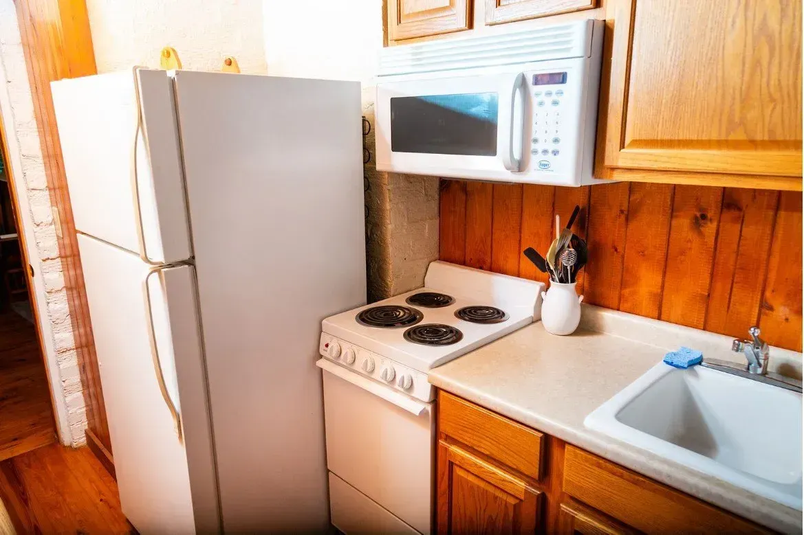Small kitchen with white appliances, microwave, and sink. Wooden cabinets and walls.