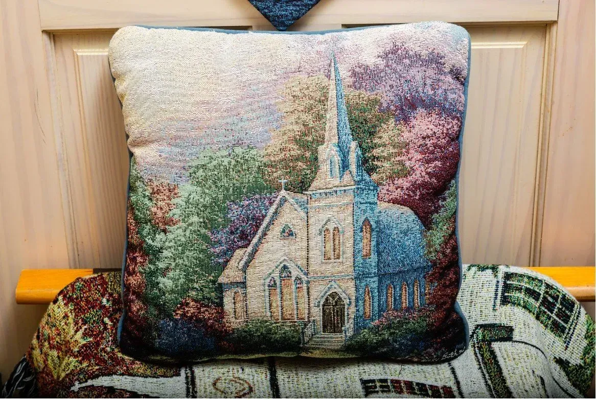 Pillow with a church scene, featuring a white building with a tall steeple, surrounded by colorful trees.