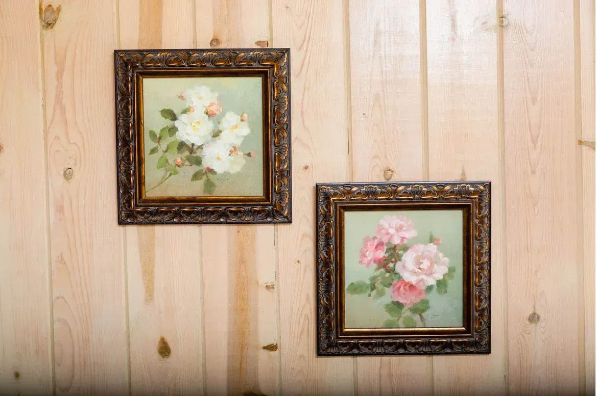 Two floral paintings with ornate brown frames hang on a light wood panel wall.