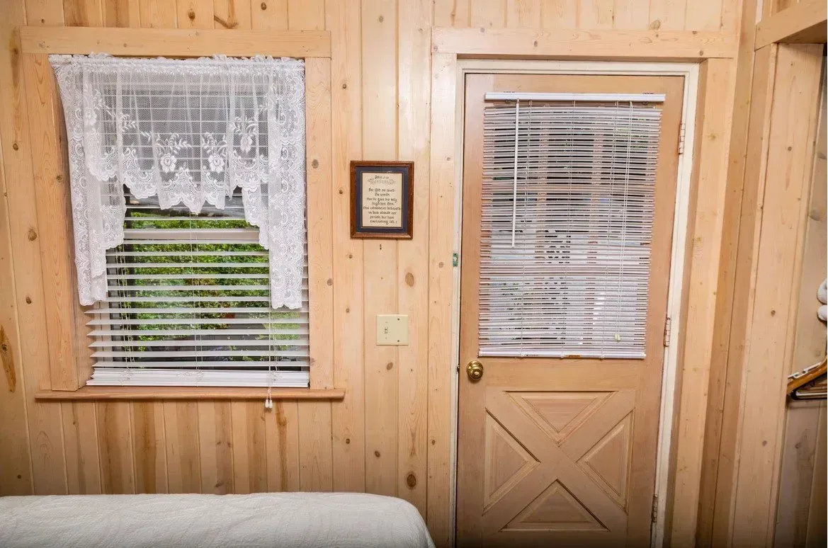 Wooden cabin interior with window, lace curtain, and door.