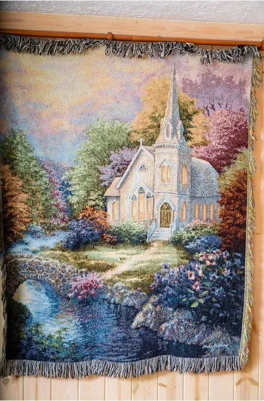 Tapestry of a church surrounded by colorful trees and a stream.