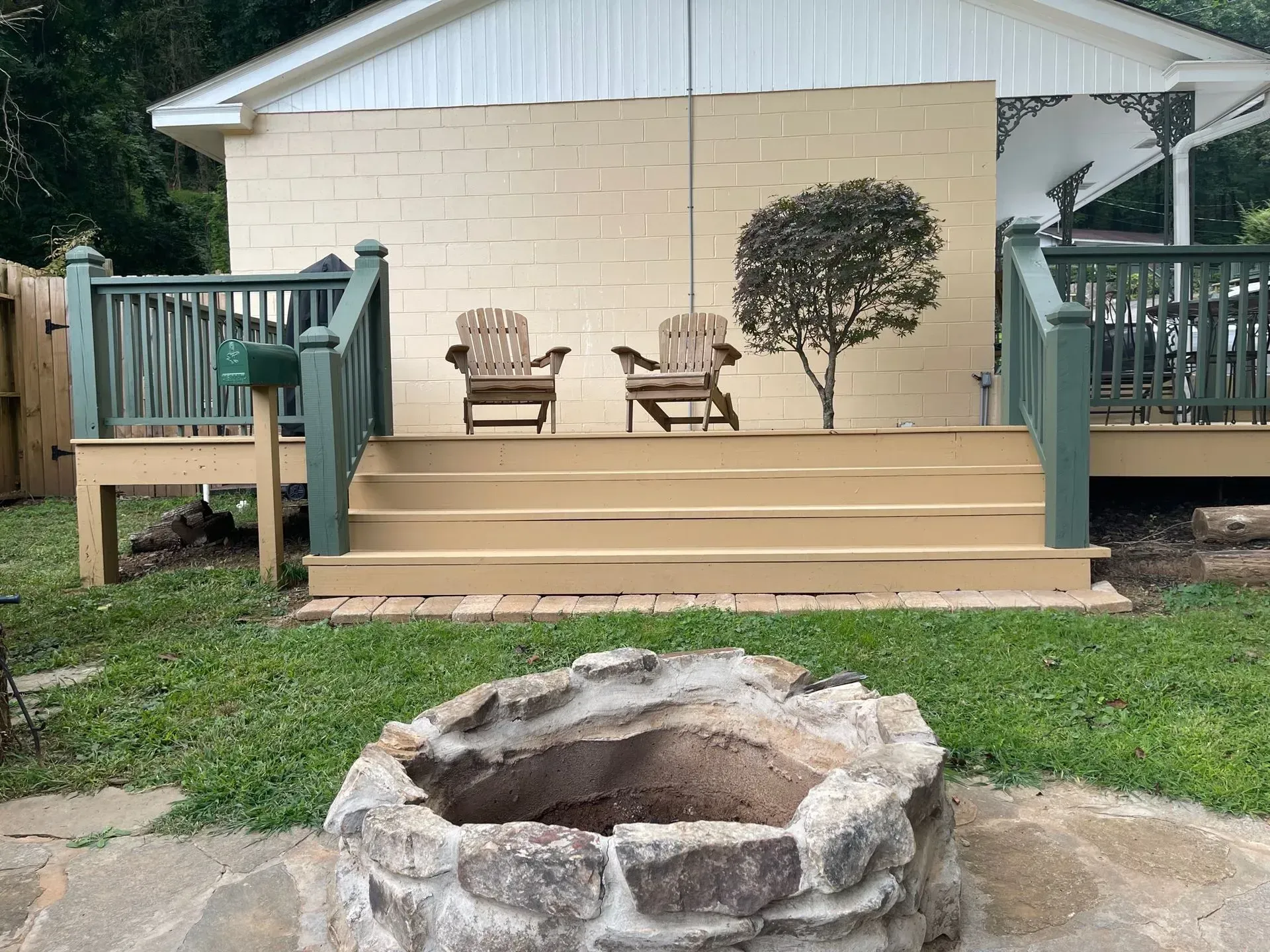 Backyard deck with chairs against a painted wall. A tree mural and stone fire pit are in the foreground.