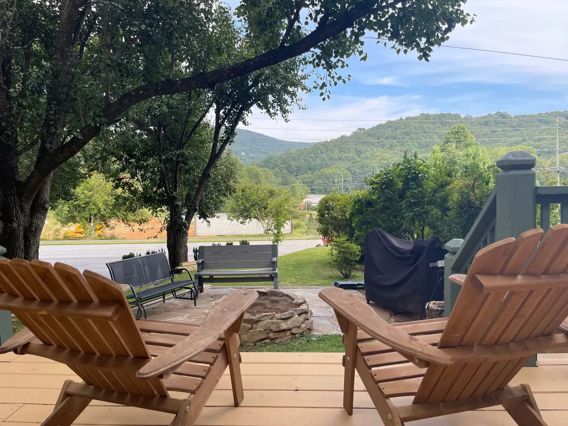 Two wooden chairs on porch overlooking a mountain view, trees, and a fire pit.