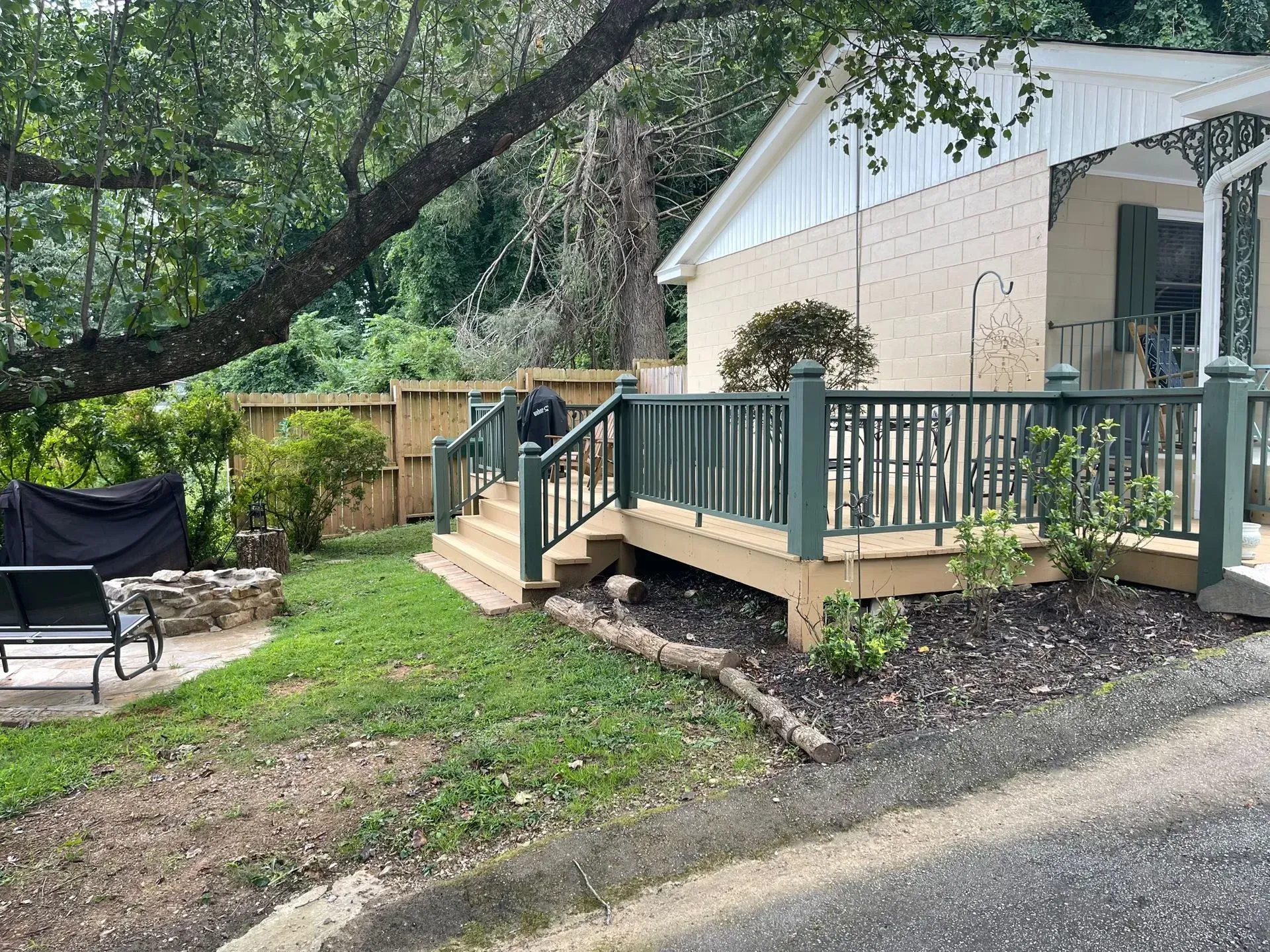 A small deck with dark green railing and stairs next to a beige building, overlooking a small yard.