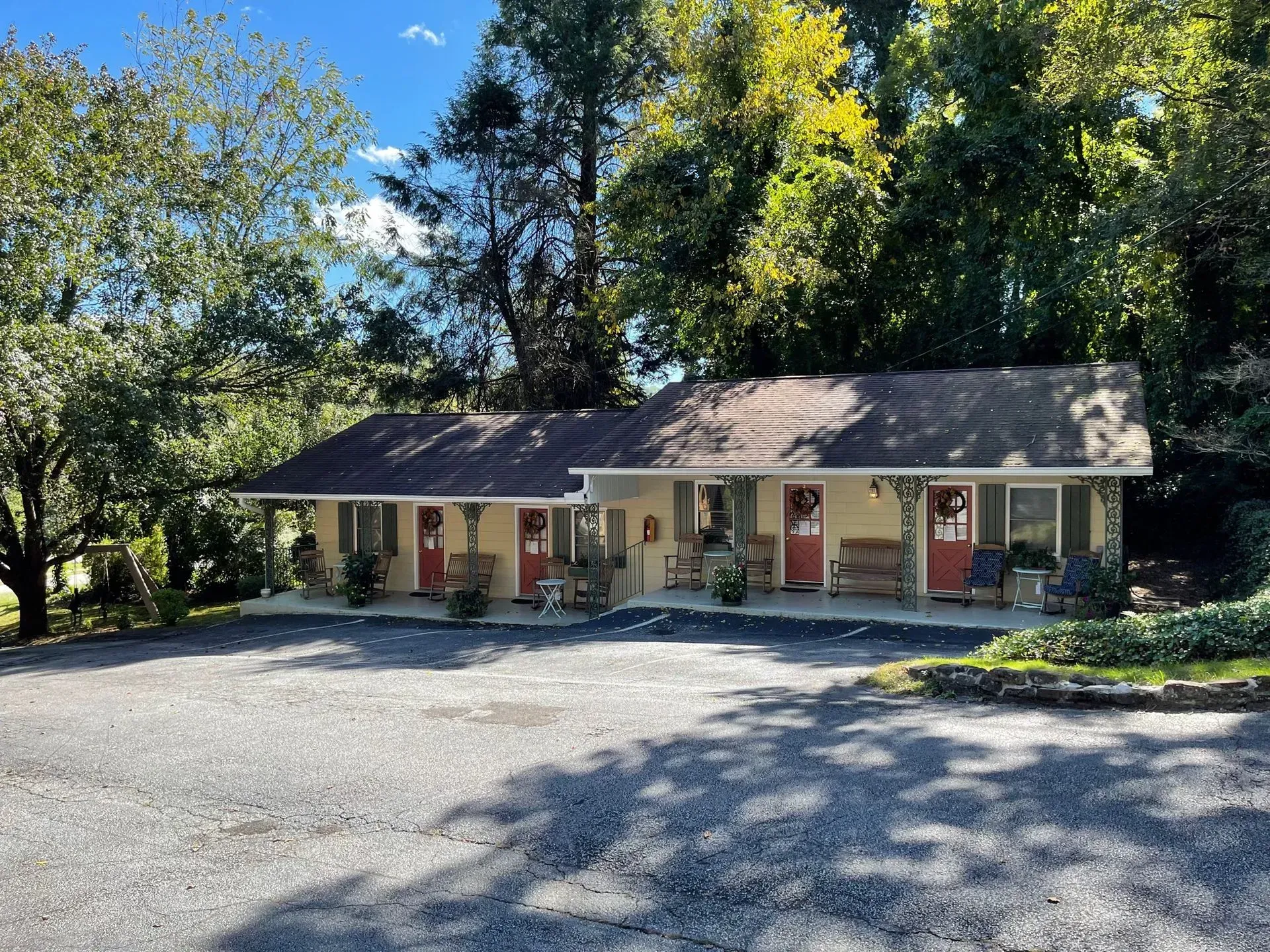 Cottage-style motel with red doors and tan siding. Gravel parking in front; trees in background.