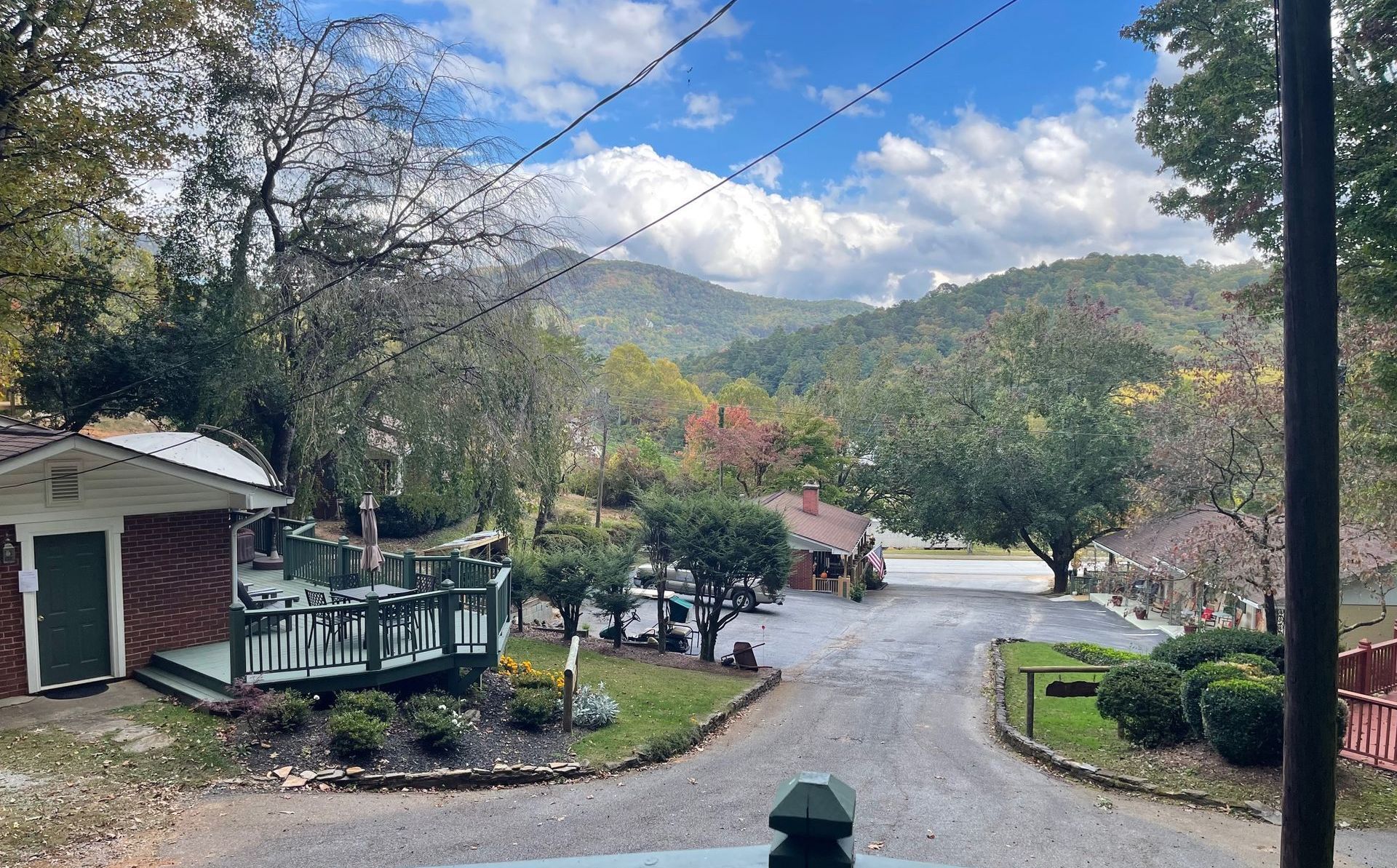 A mountain view from a gravel road, with buildings and trees in the foreground. Overcast skies.