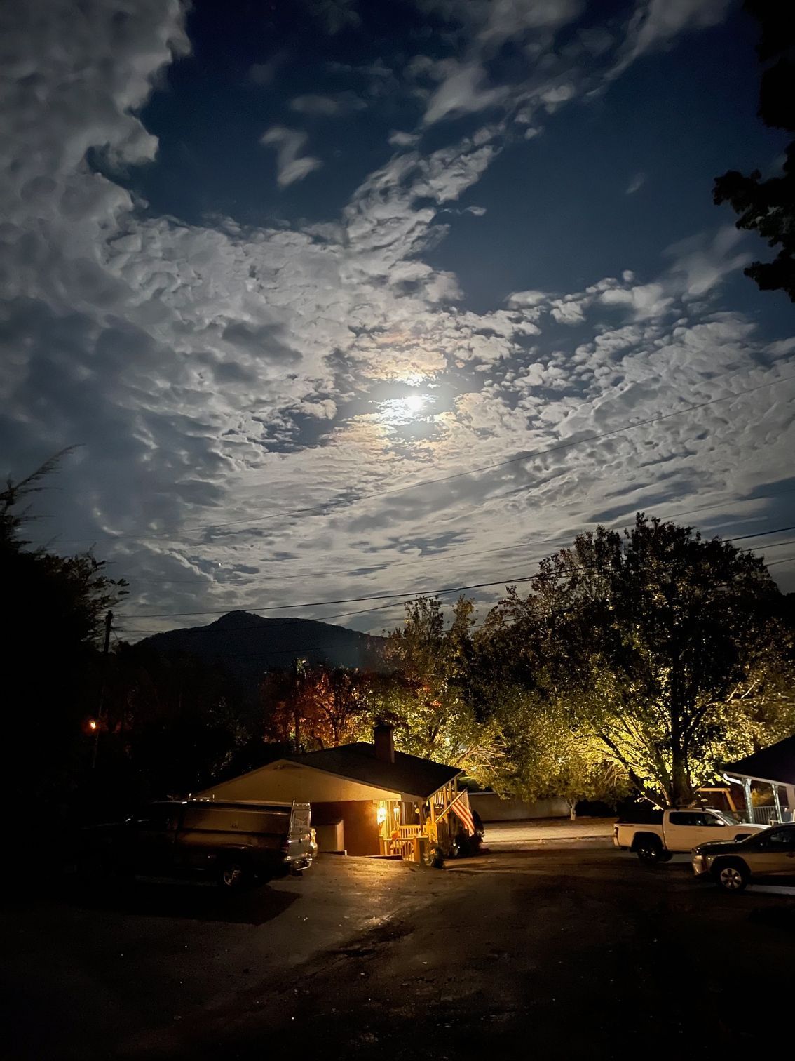 Night scene: a house illuminated, full moon peeking through clouds, dark landscape.