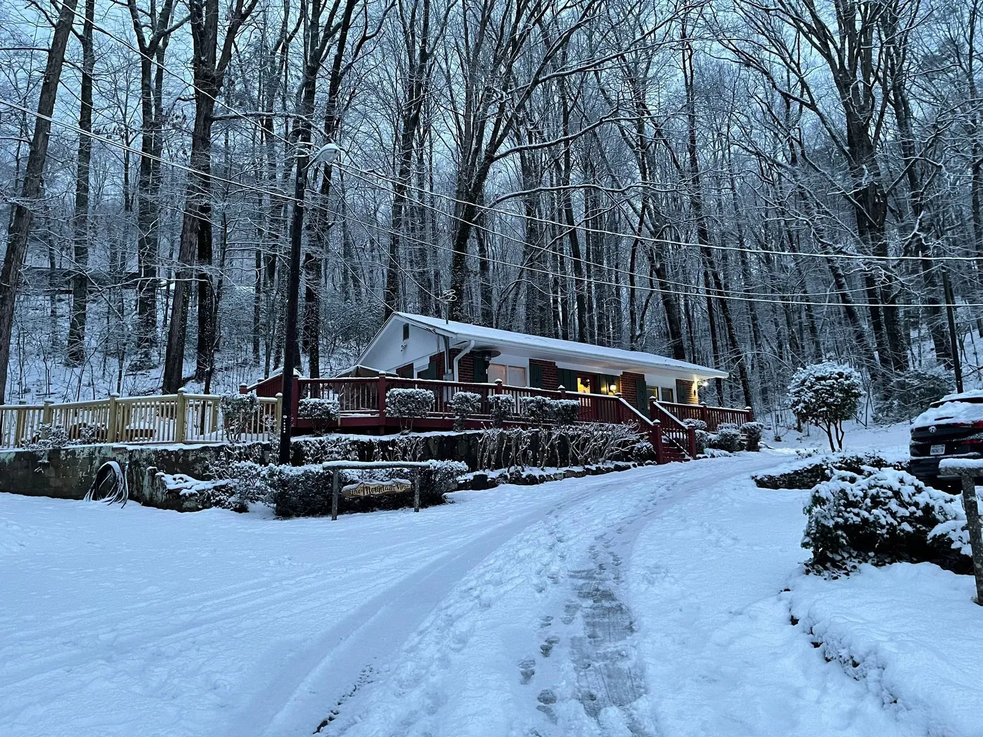 Snow-covered cabin in a forest, surrounded by bare trees. White snow on the ground and roof, red deck, overcast lighting.