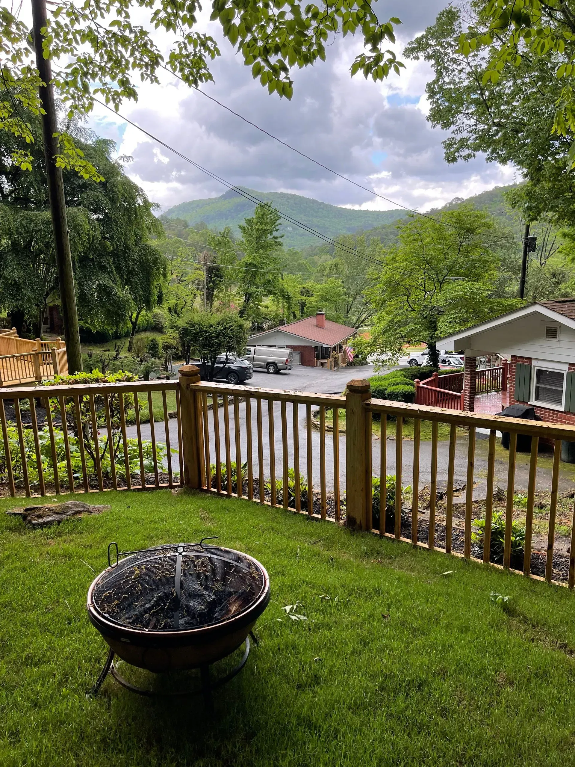 Lush green yard with a fire pit overlooking a valley and distant mountains on a cloudy day.