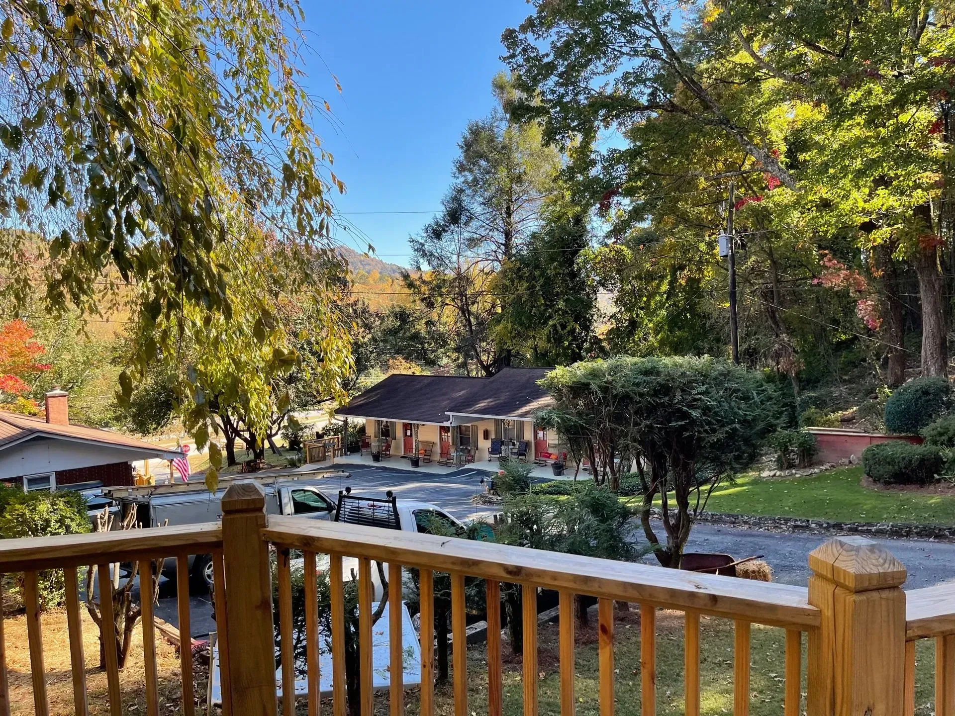 View from a wooden deck of a building with a long porch, surrounded by trees and blue sky.