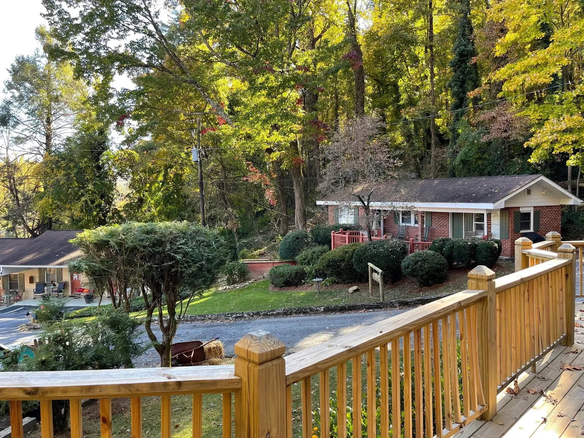 Wooden deck overlooking a small cabin with red and white brick, surrounded by green bushes and trees.
