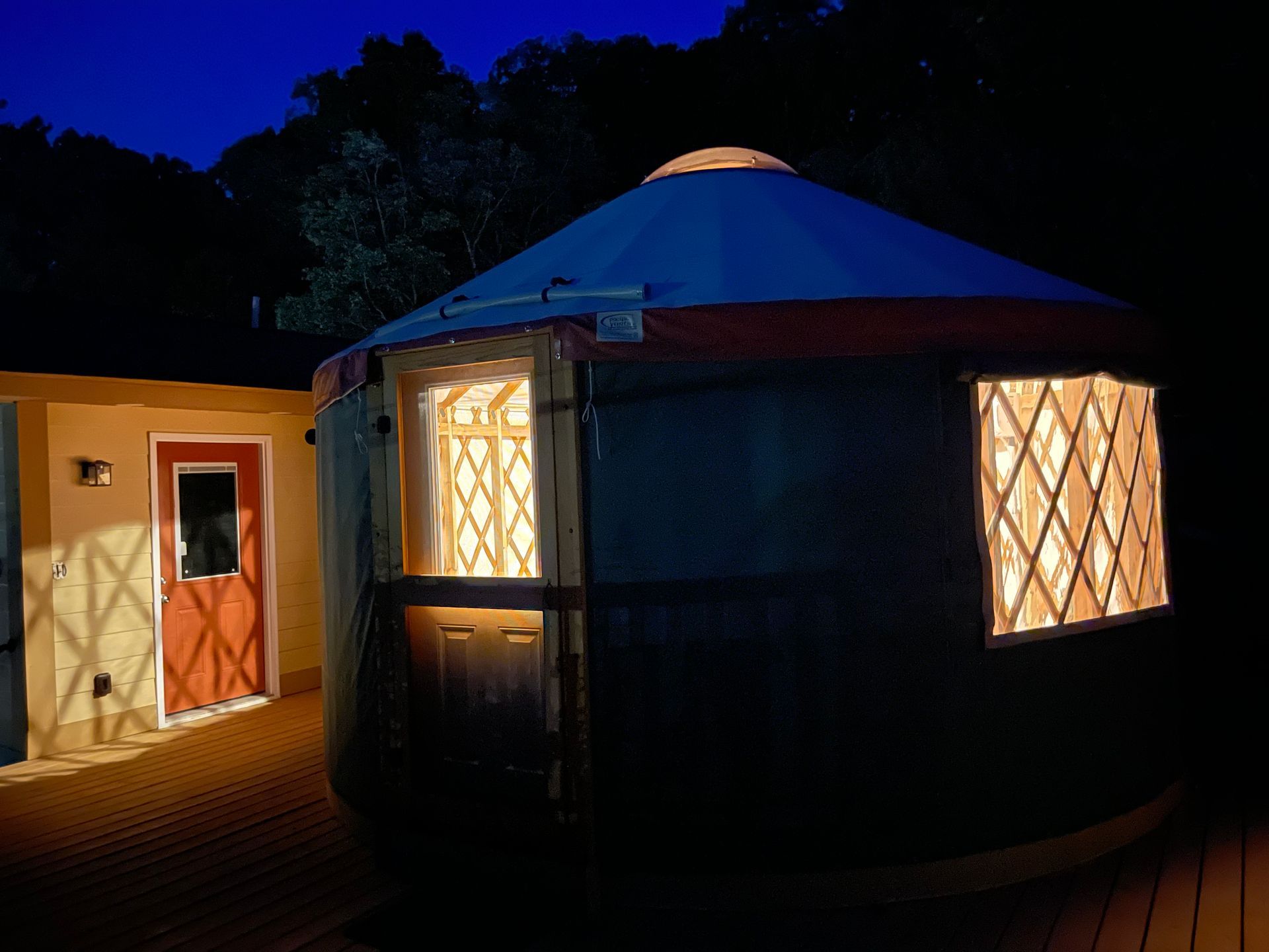A lit-up yurt with a doorway and a window on a deck at night.