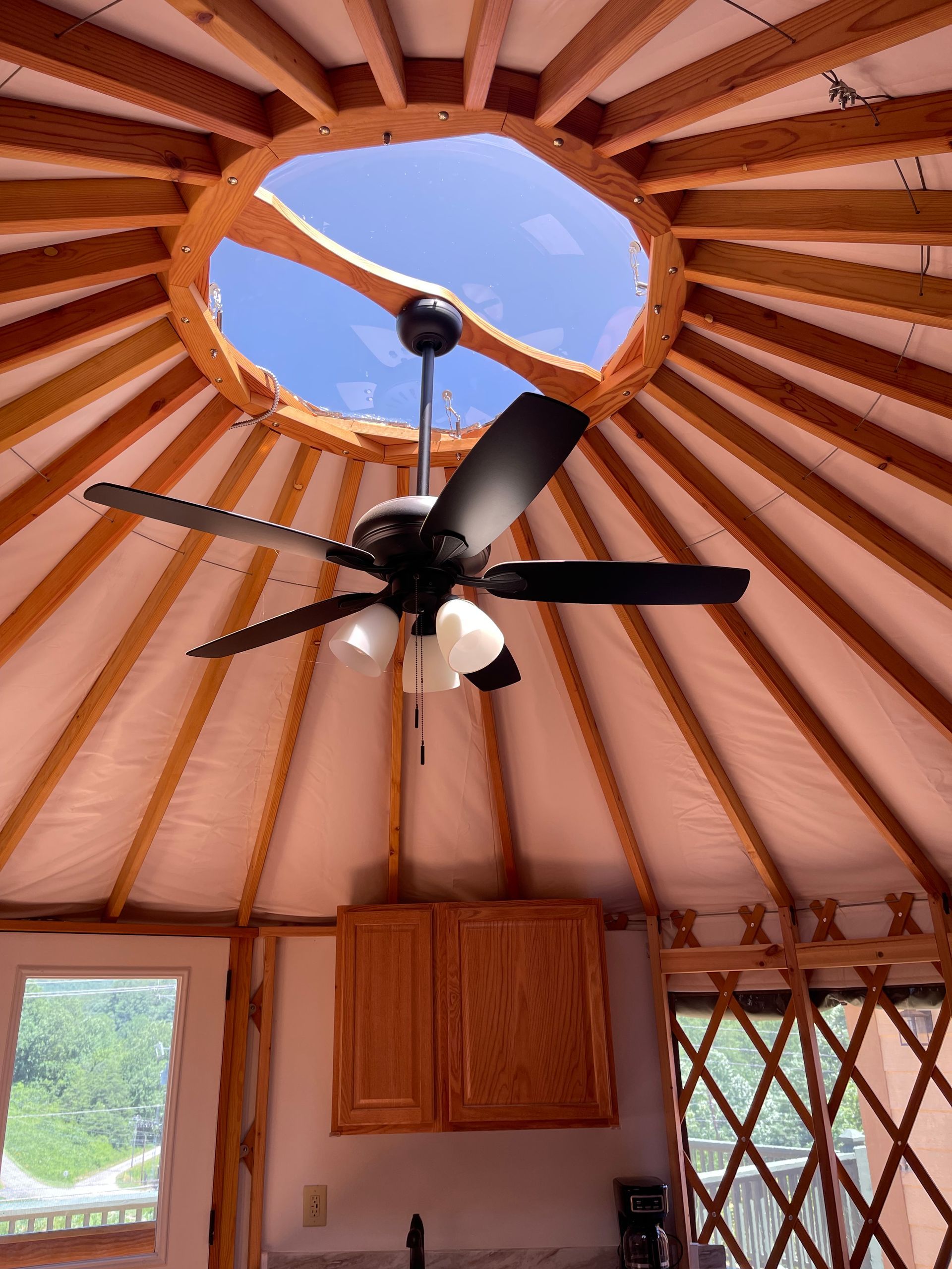 Interior of a yurt with a ceiling fan, skylight, and wooden cabinets.