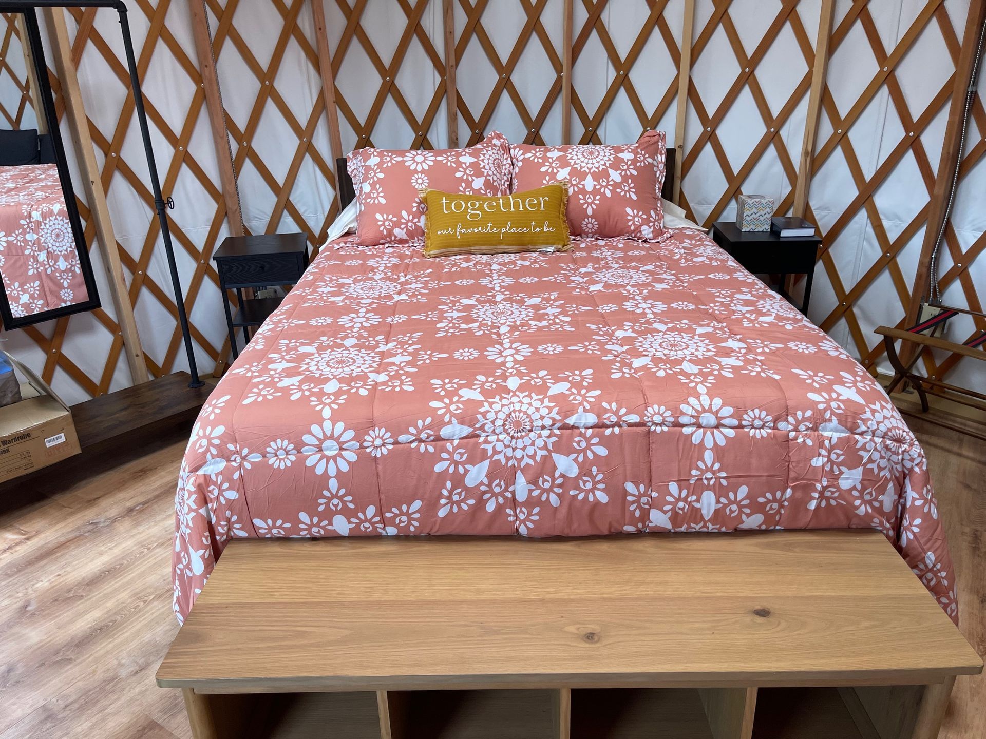 Bed in a yurt; peach floral bedding, wooden furniture, and a gold pillow with text.
