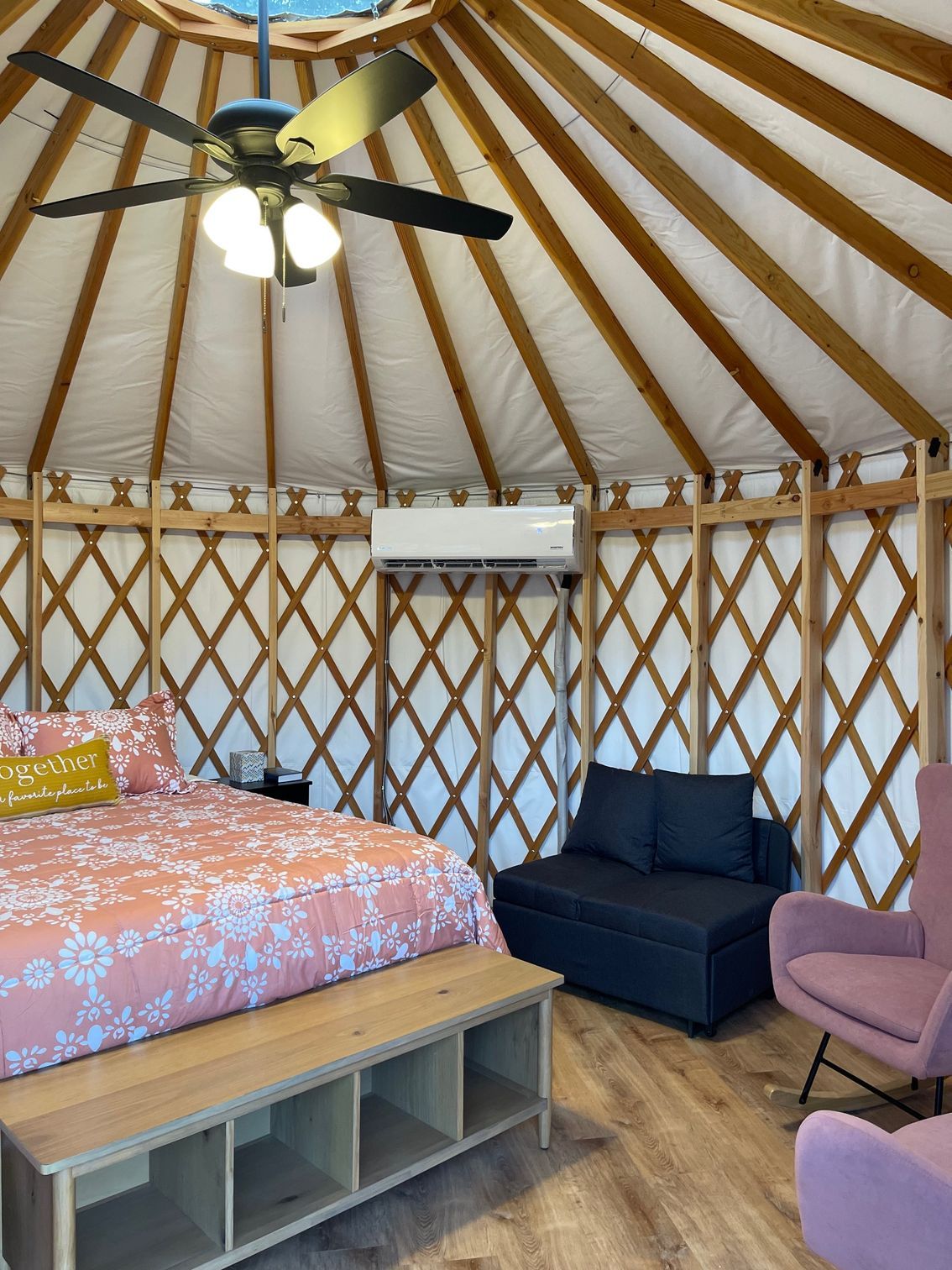 Interior of a yurt bedroom with bed, seating, ceiling fan, and air conditioner.