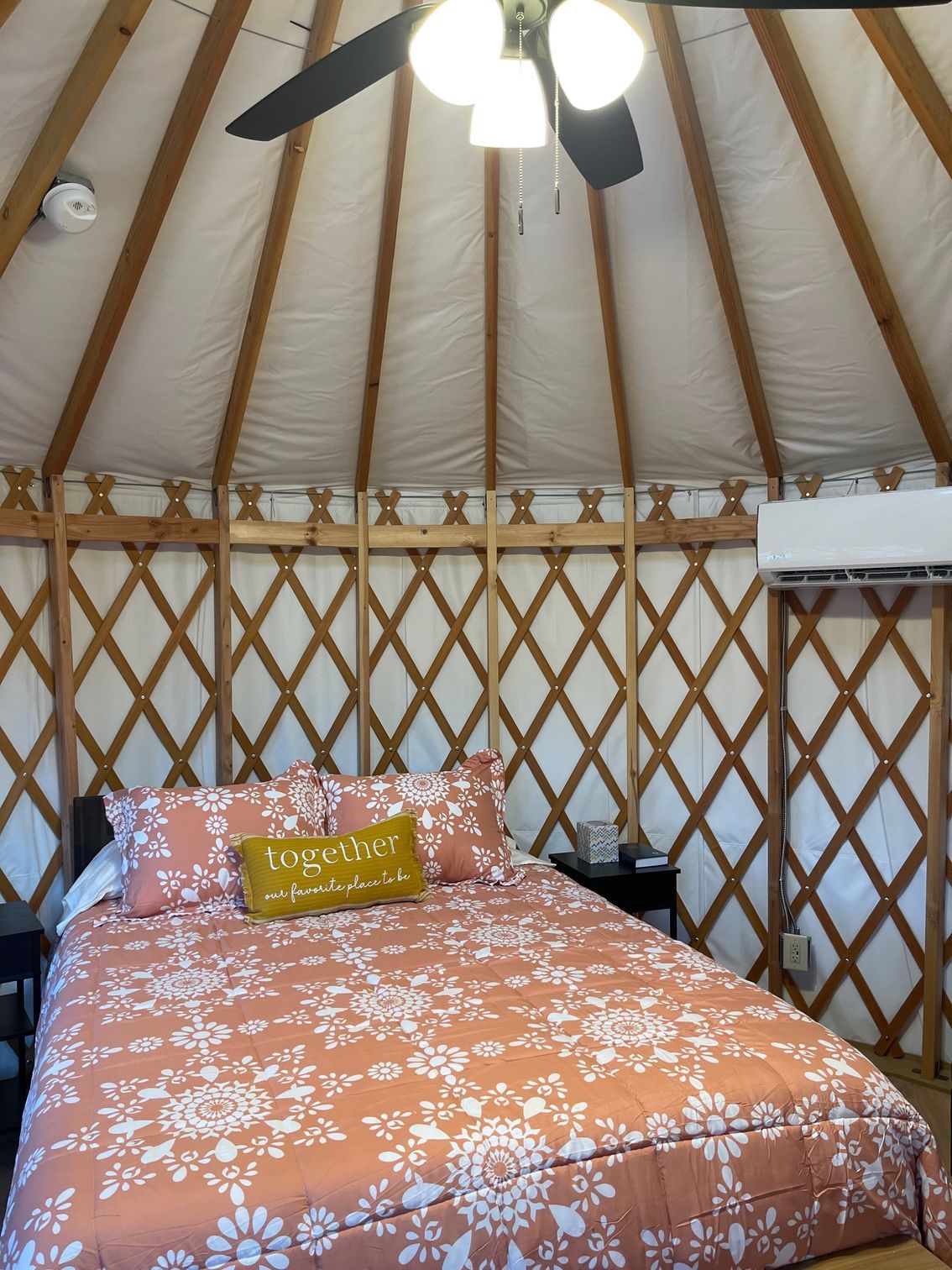 Interior of a yurt with bed covered in orange and white patterned bedding. Ceiling fan overhead.