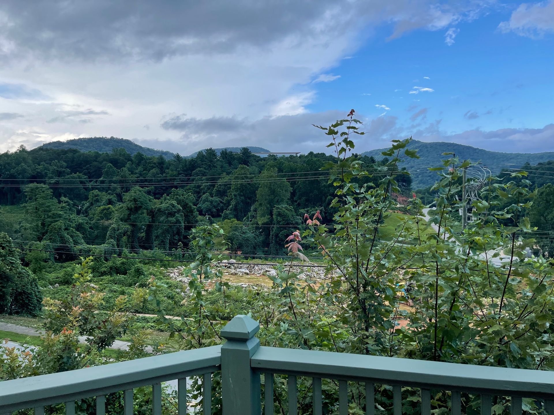 A view of lush green mountains and trees under a cloudy sky, seen from a deck.