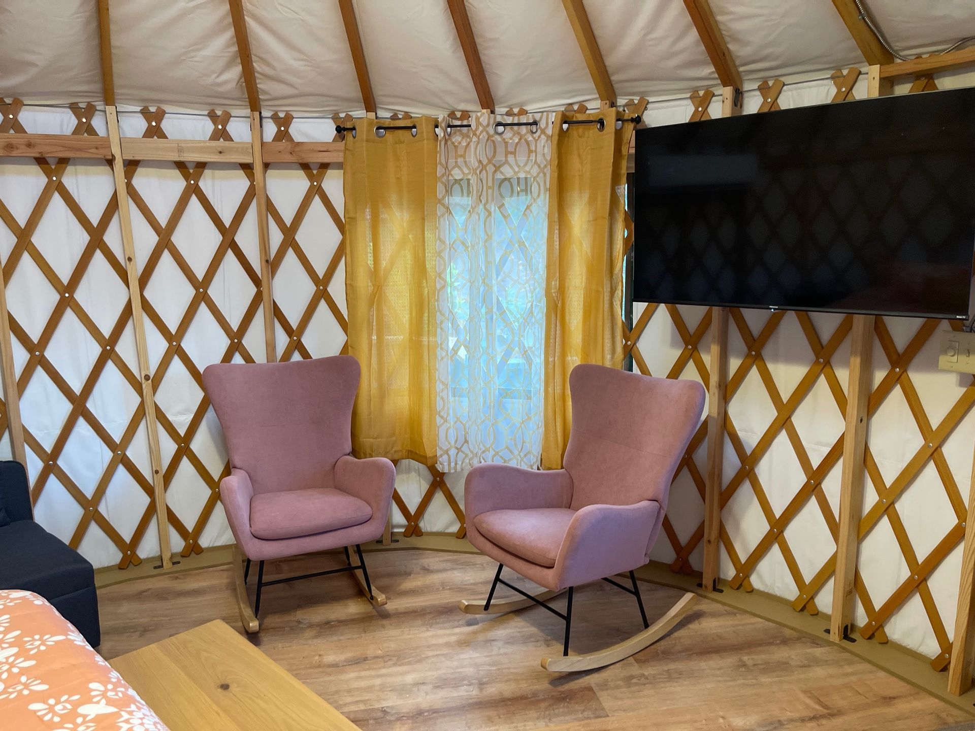 Two pink rocking chairs face a window in a yurt with a TV on the wall.