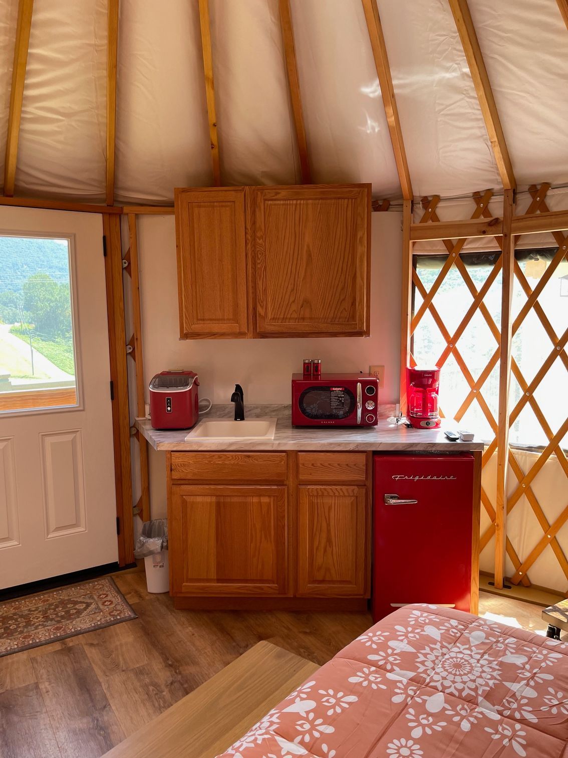 Interior of a yurt with a kitchenette, including a red microwave and fridge, cabinets, and a sink.