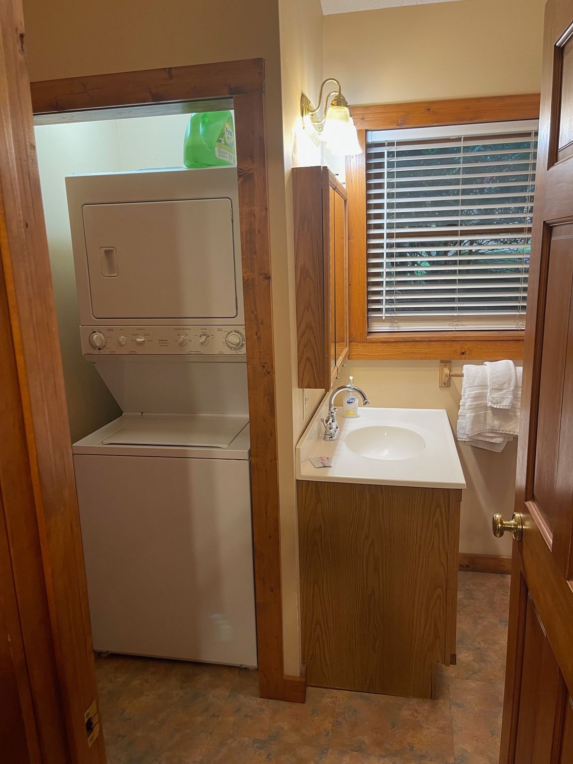 Stackable white washer and dryer in a wood-framed alcove, next to a bathroom sink.