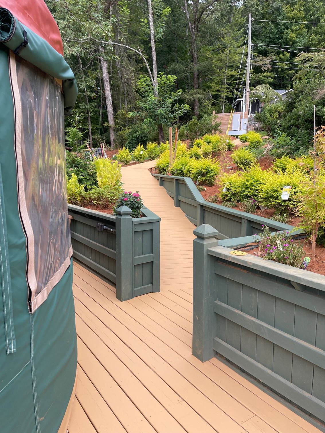 Wooden deck and walkway bordered by green planters, leading to a wooded area.