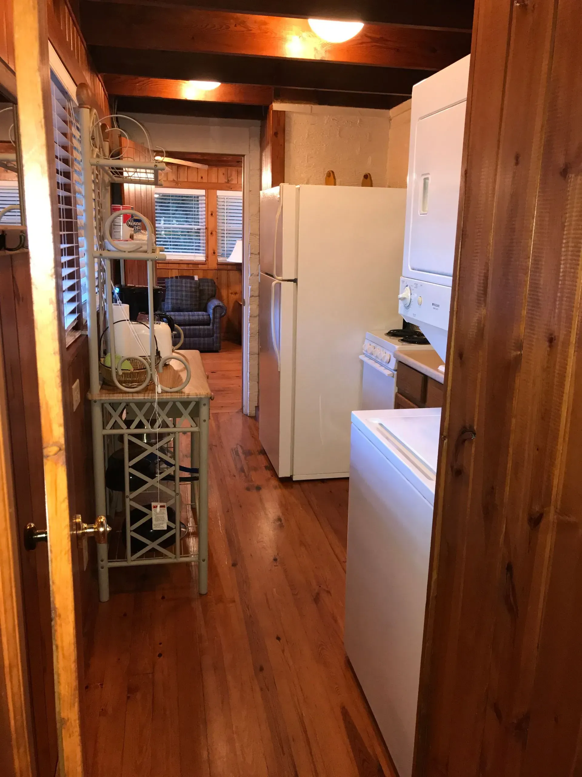 Narrow kitchen with appliances and wood flooring leading to living area.