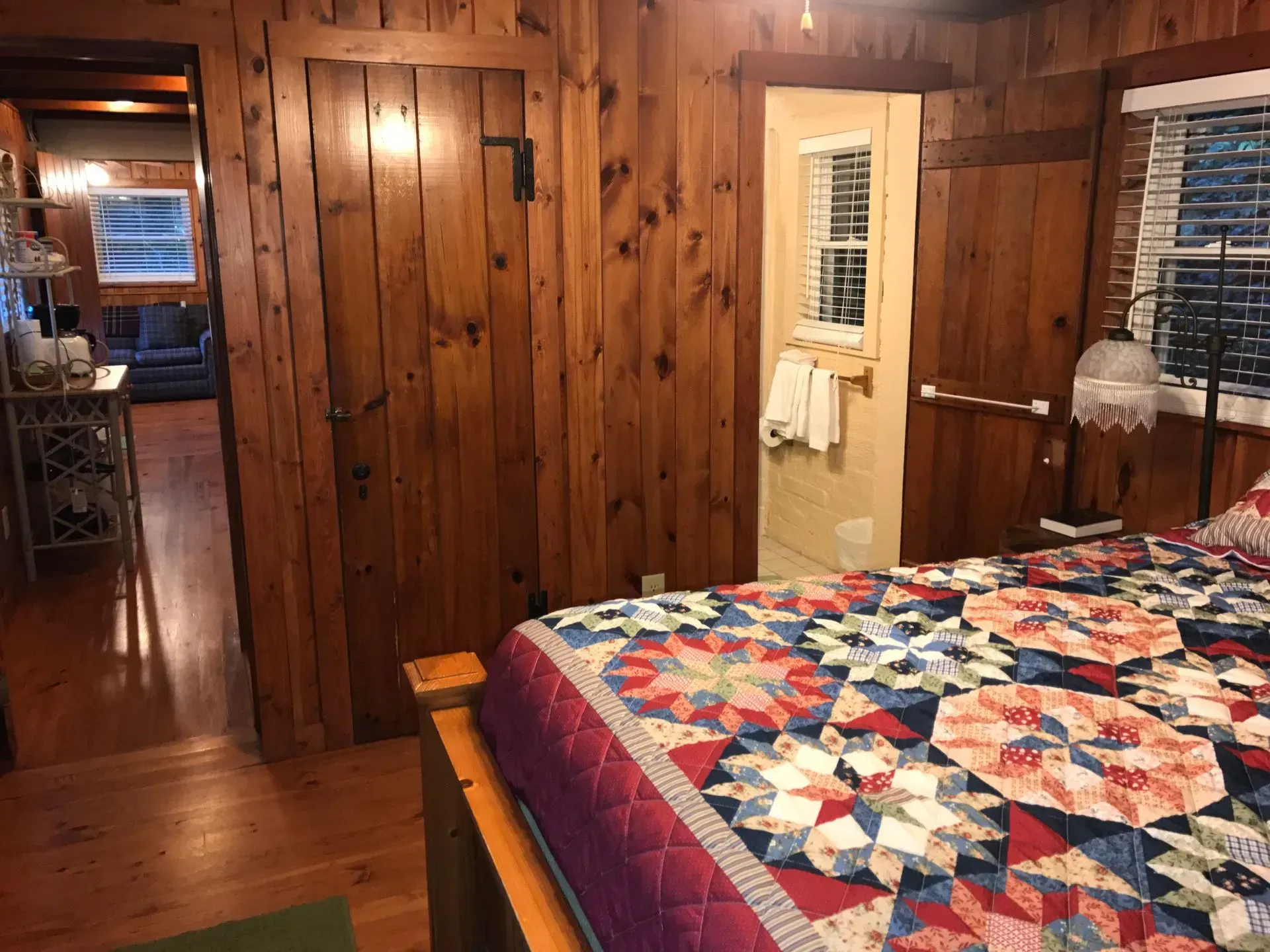Bedroom with wooden walls, bed with quilt, doorway to bathroom and hallway.