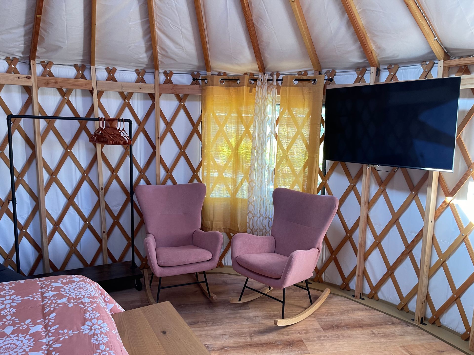 Interior of a yurt with two pink rocking chairs, TV, and wooden frame structure.