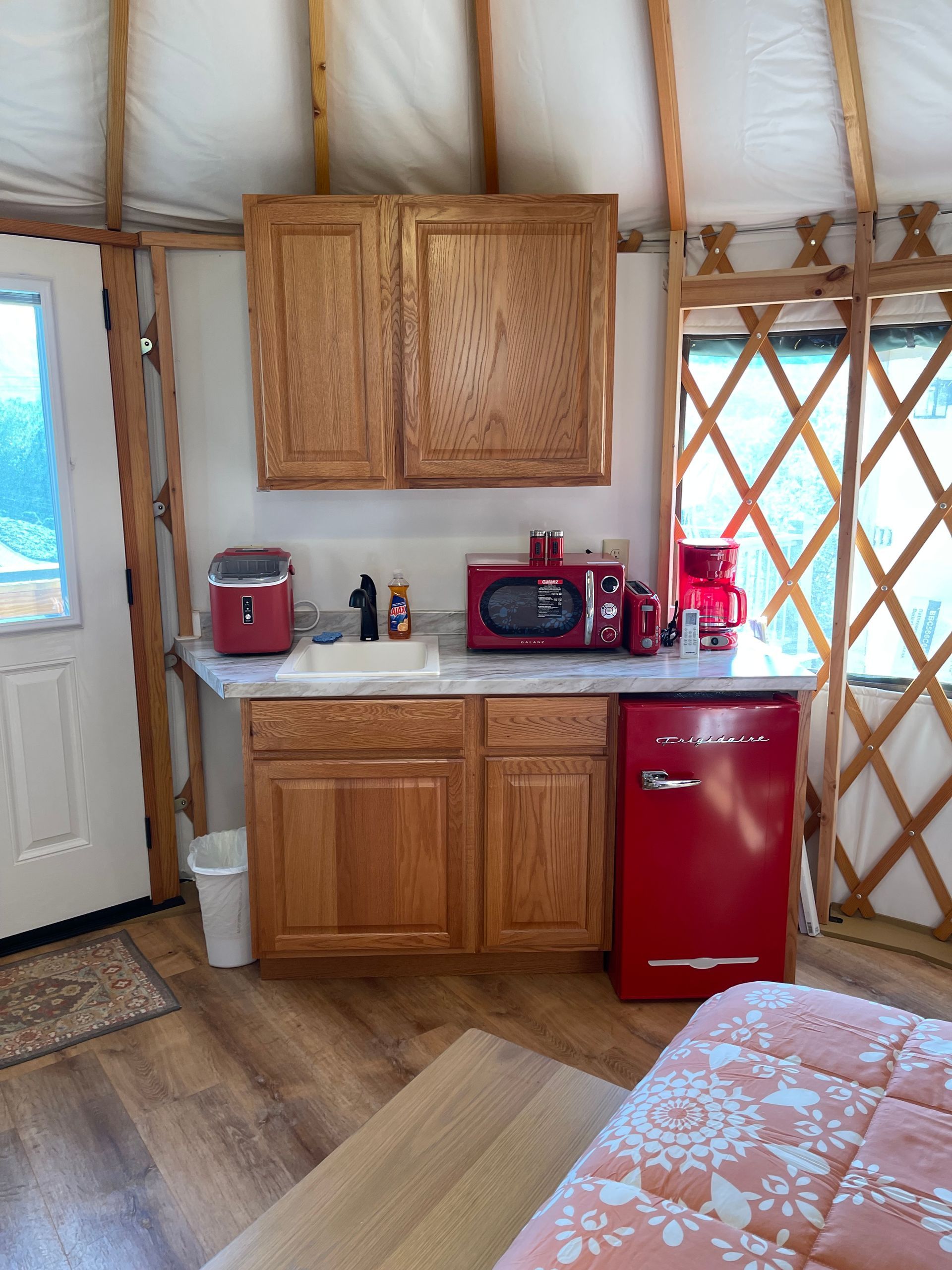 A yurt kitchen with red appliances, wooden cabinets, and a small sink.