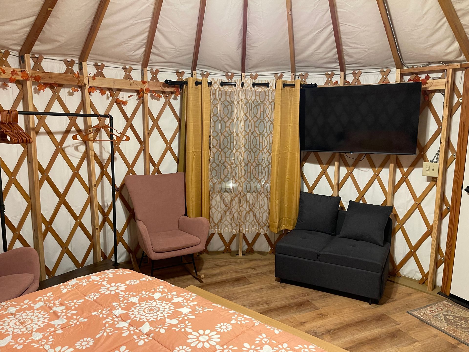 Interior of a yurt with two pink rocking chairs, TV, and wooden frame structure.