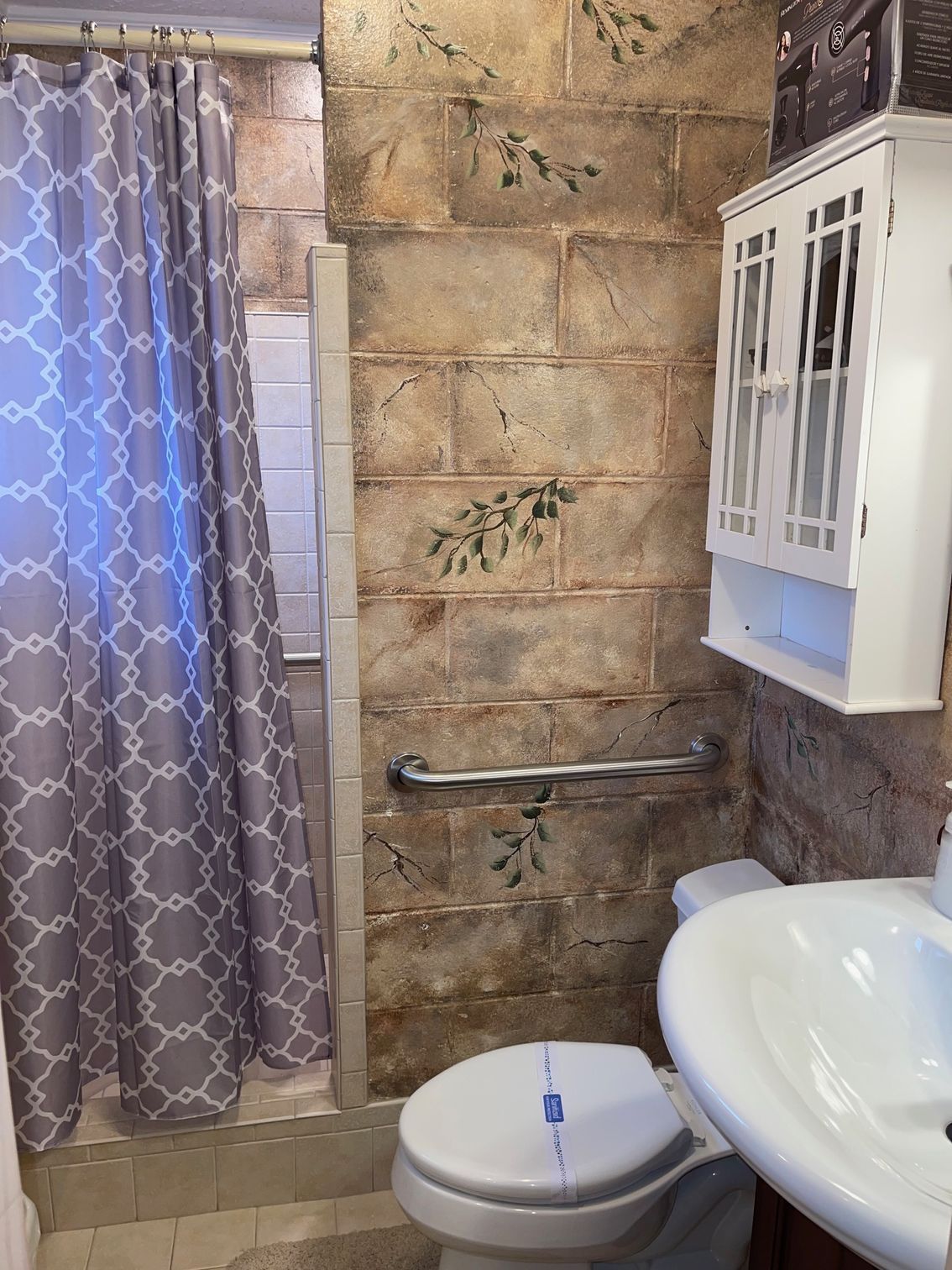 White wall-mounted cabinet with glass doors and shelf on a textured brown wall, adorned with green vines.