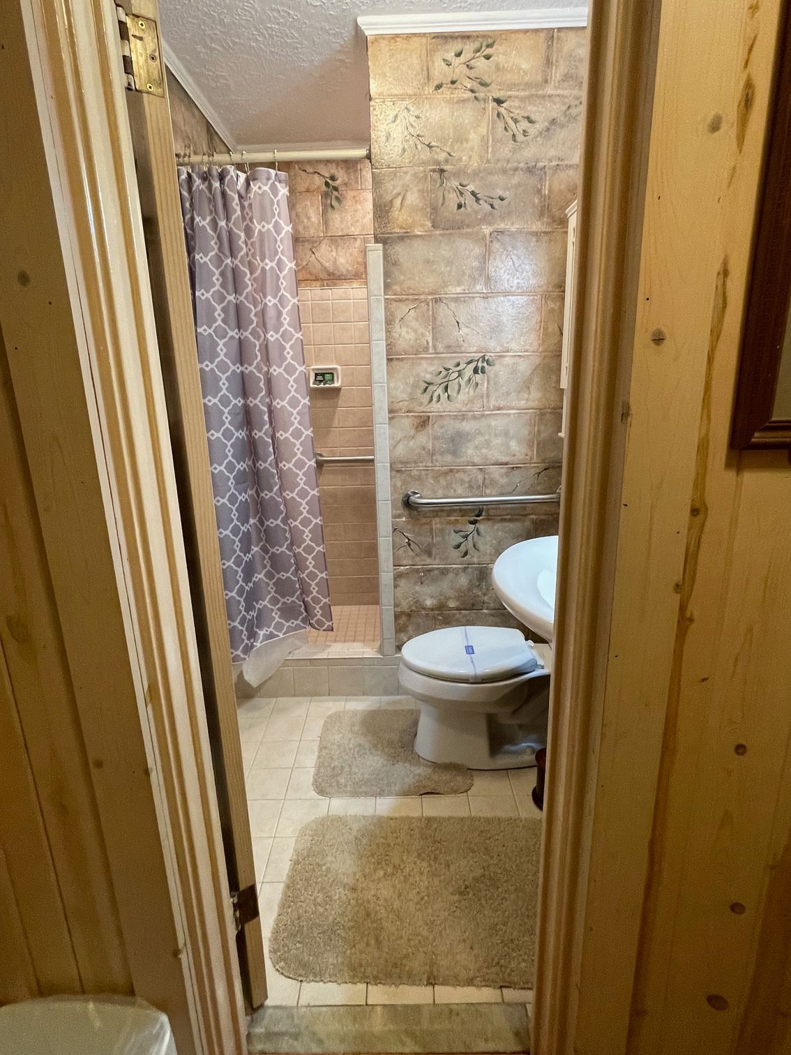 White cabinet with glass doors and greenery, mounted on textured wall in a bathroom.