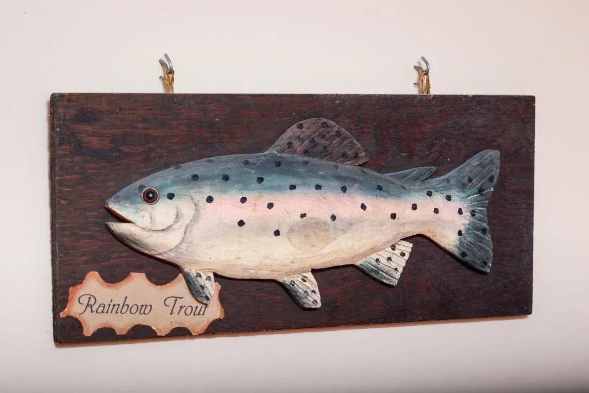 Wooden plaque with a carved, painted rainbow trout; brown background, beige label: