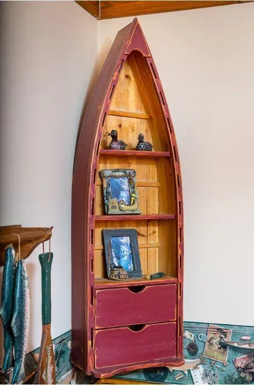 Maroon boat-shaped bookshelf in a corner, filled with decor.