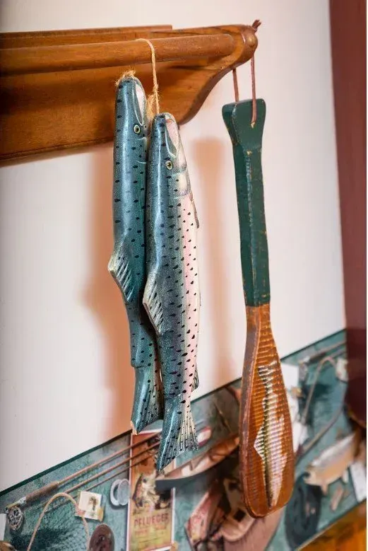Three blue fish and a wooden paddle hanging from a wooden shelf against a wall.