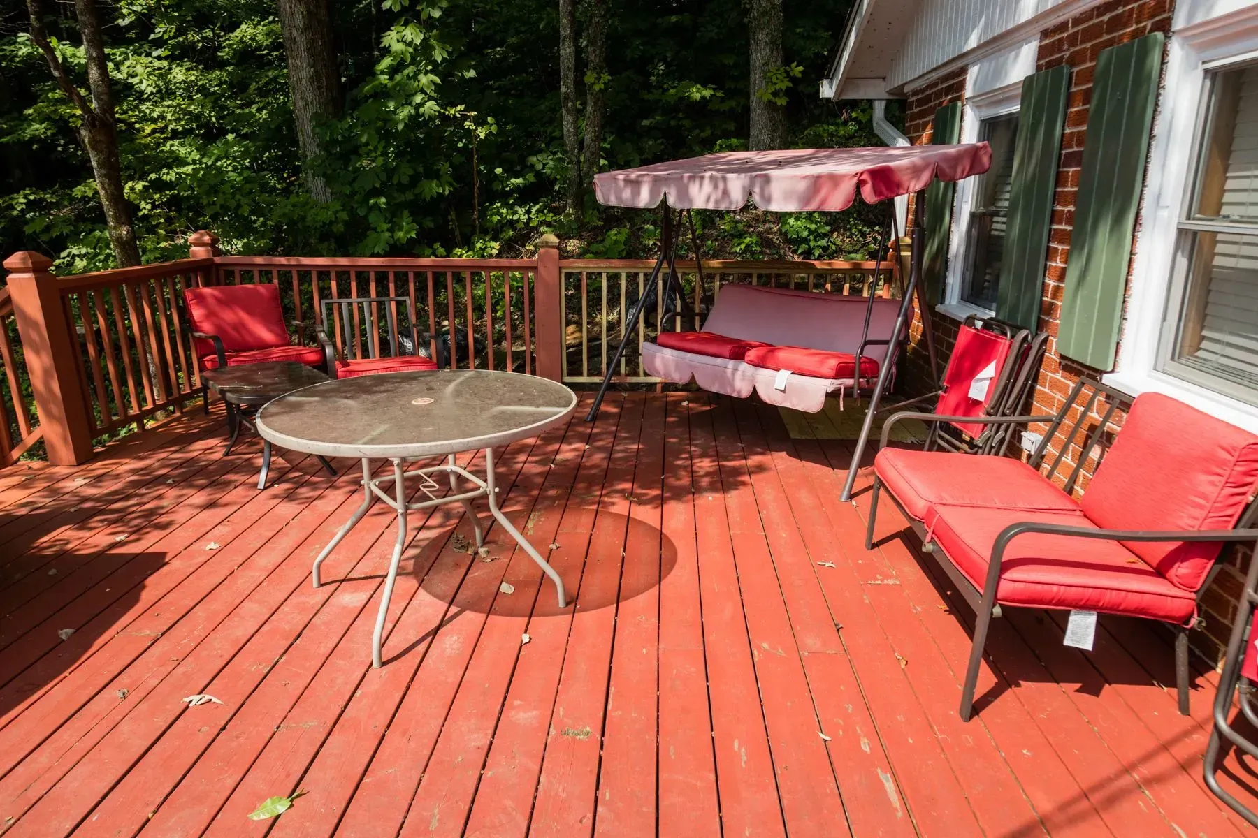 Red painted deck with outdoor furniture: table, chairs, swing, and forest background.