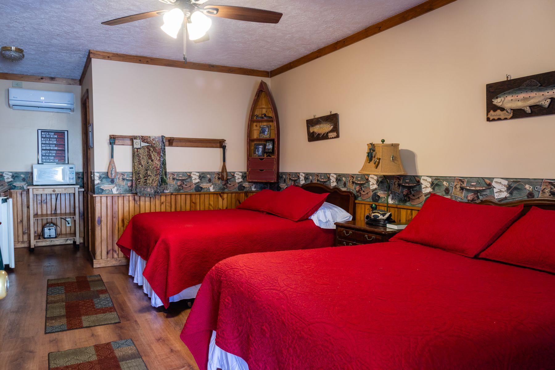 Two beds with red bedding in a wood-paneled room, decorated with fishing-themed art.