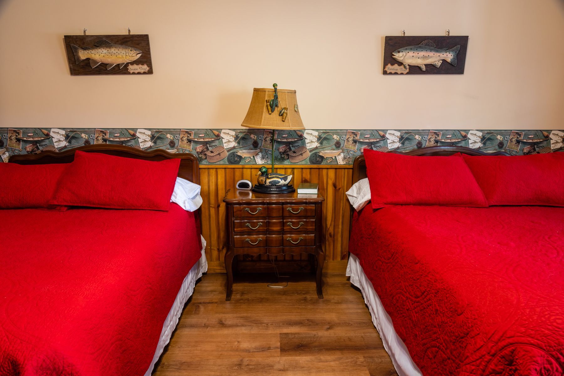 Two red-covered beds in a bedroom with a nightstand between them, decorated with fish art.