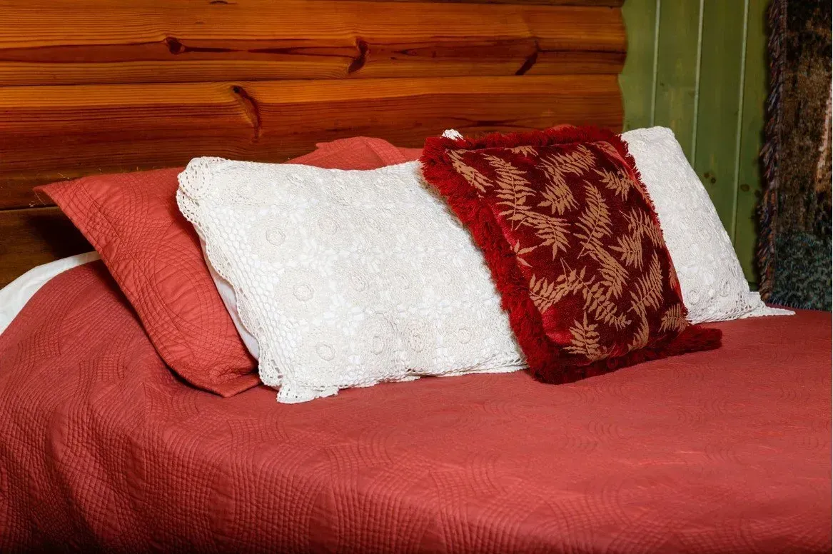 Red bed with white and red pillows against a wooden headboard.