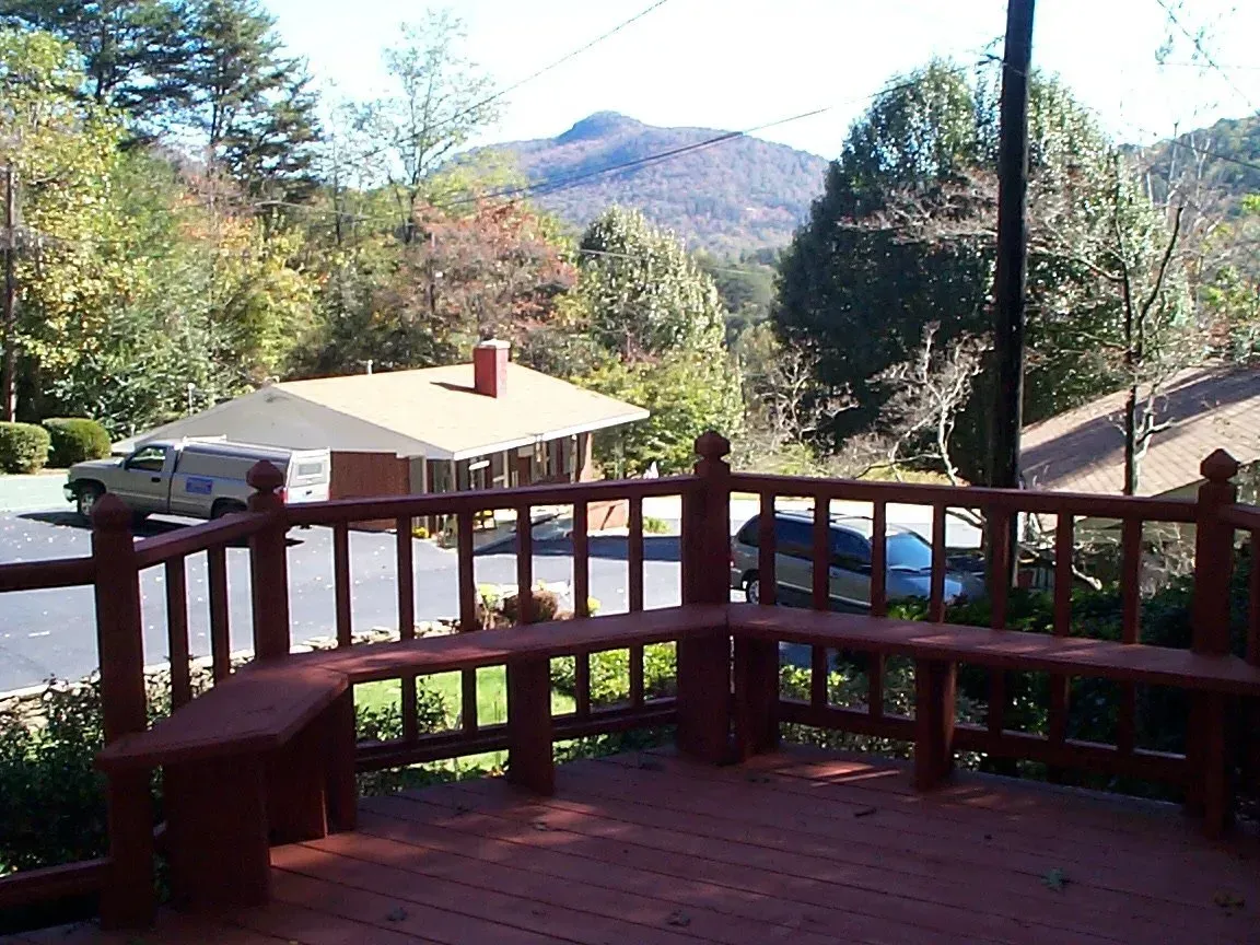 Wooden deck with bench overlooking a mountain and a building with a red brick chimney.