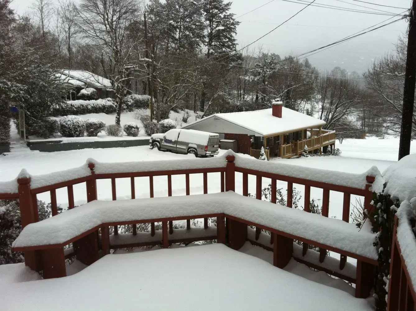 Snow-covered deck with benches overlooking a house and trees blanketed in snow.