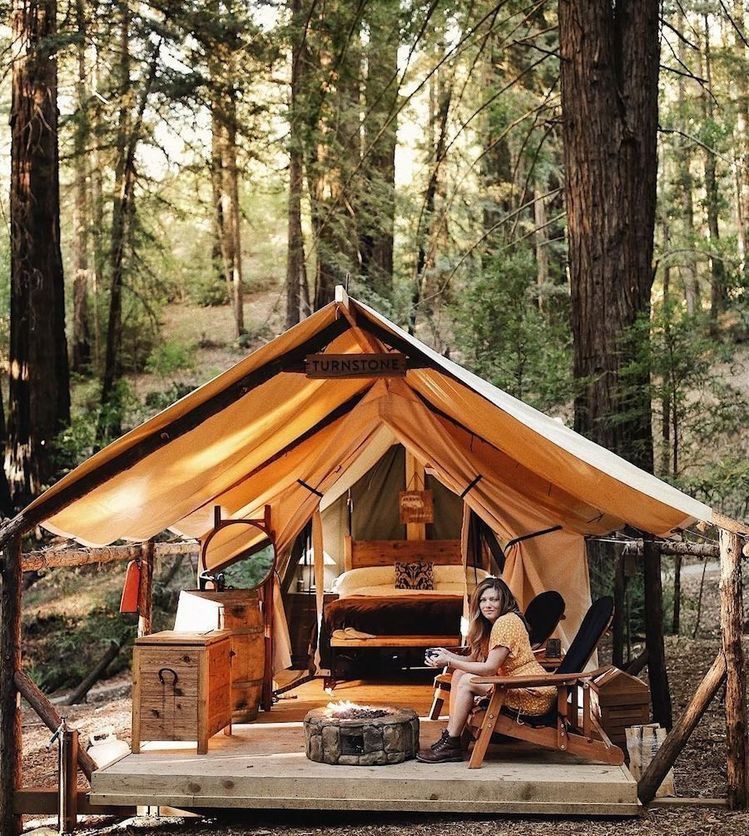 Woman sitting in a lounge chair outside a glamping tent in a forest.