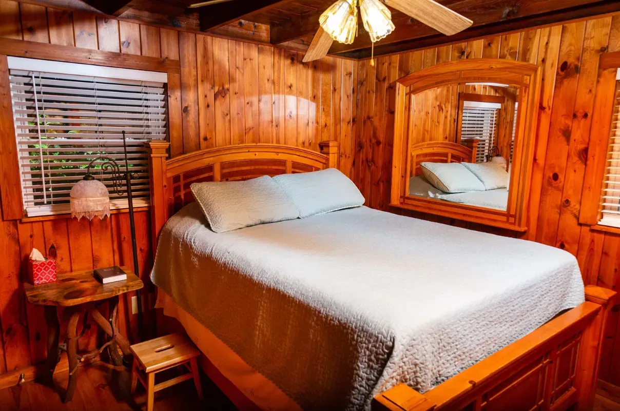 Bedroom with wooden walls, bed, mirror, and window with blinds.