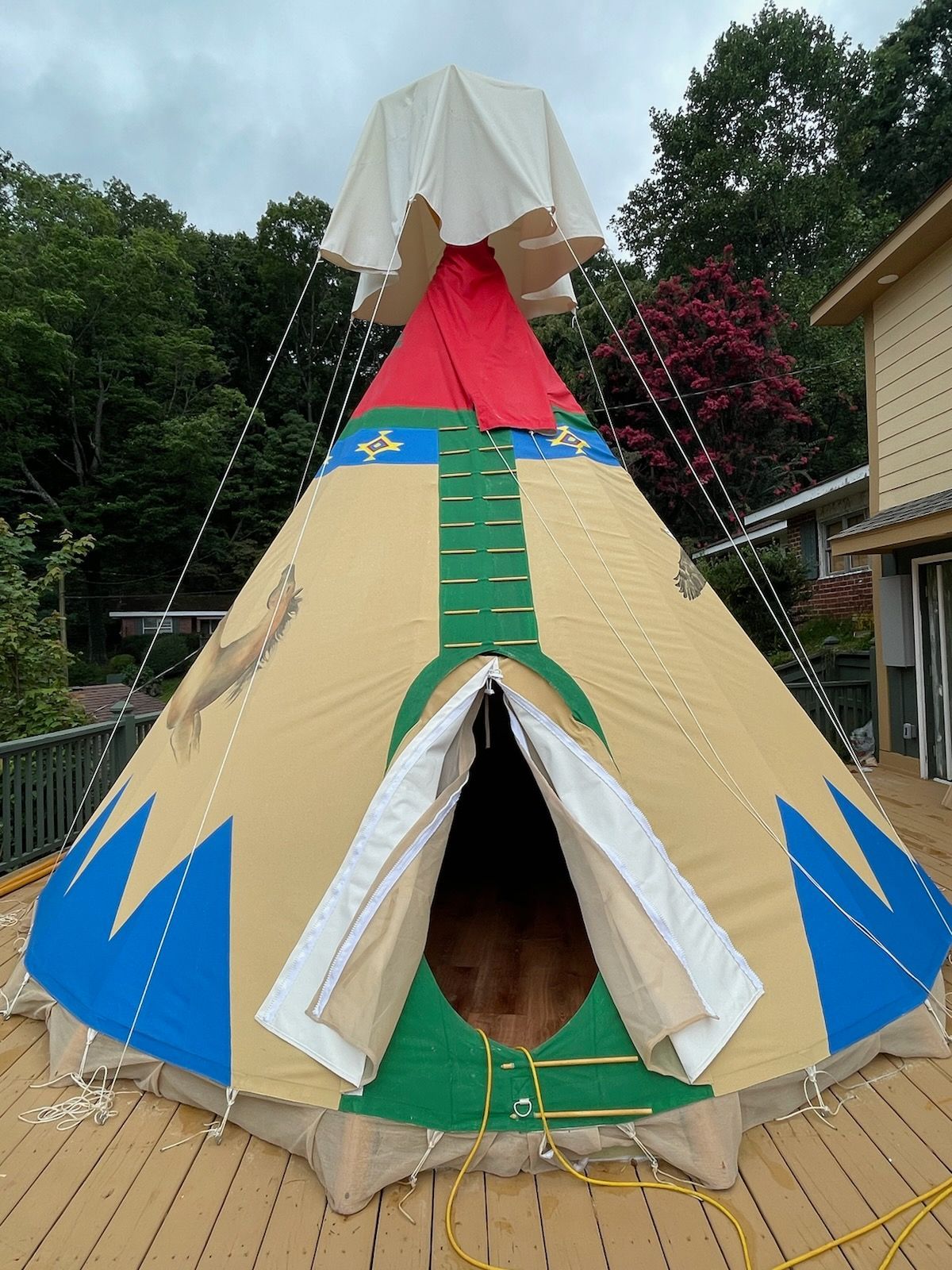 Tan tipi tent with blue, green, and red accents, set on a wooden deck outdoors.